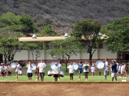 A student marching band plays drums on their school field.