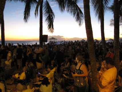 The sun sets behind the crowd gathered on Waikiki Beach.