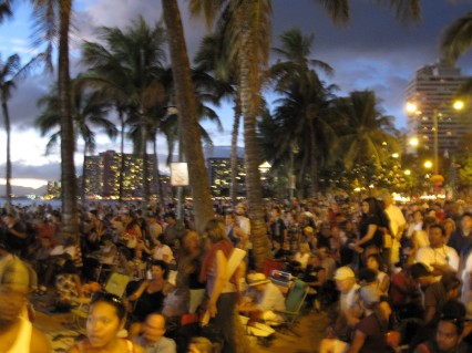 The hotels lining Waikiki Beach light up the night sky and serve as the backdrop for the crowd gathered on Queen's Beach.