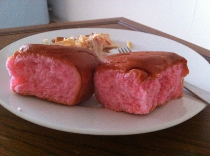 Two pink-colored dinner rolls sit on a white plate