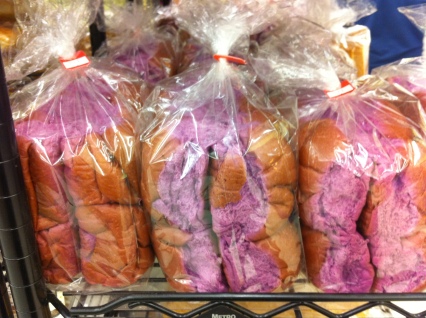 Clear plastic bags hold bright-purple-colored dinner rolls on a supermarket shelf